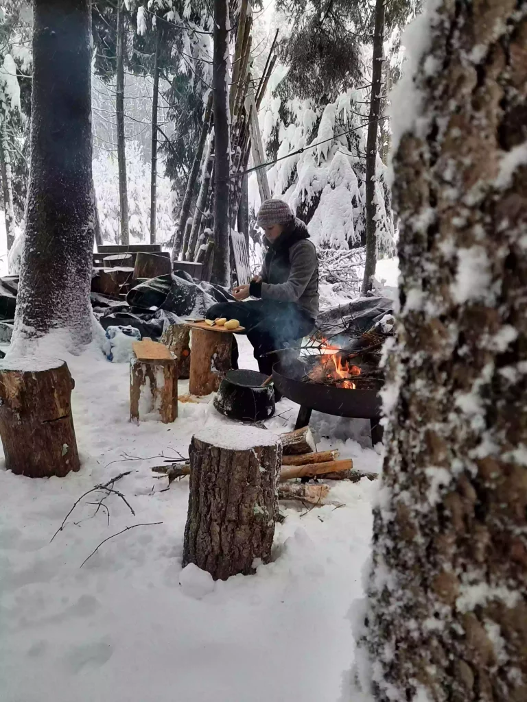 Eine Frau kocht am Lagerfeuer im Winterwald